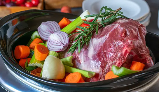 Slow cooker full of raw meat and vegetables preparing to cook