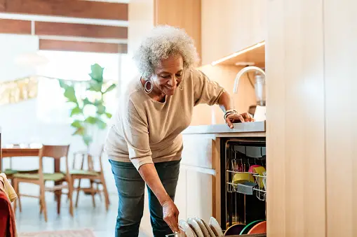 Older woman loading the dishwasher at home