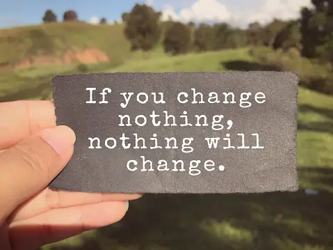 Female hand holding a motivational sign that says if you change nothing, nothing will change