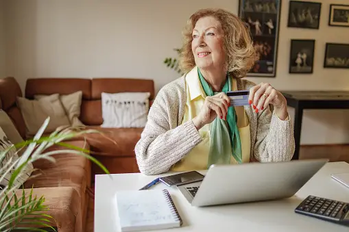 Older woman sitting at computer holding a credit card