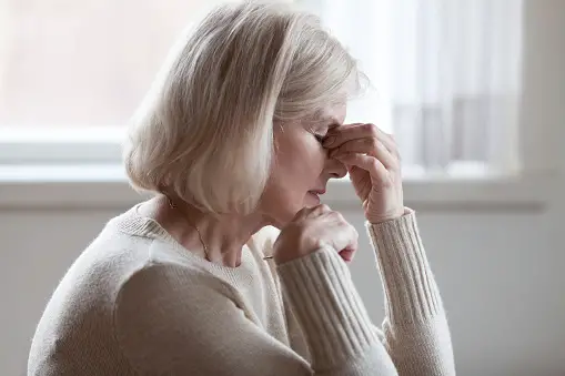 Side profile of older woman with one hand on chin and the other close to her forehead, looking upset