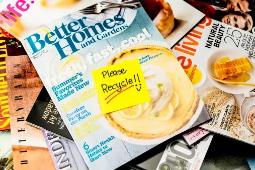 Stack of magazines with yellow sticky outlining 'please recycle'