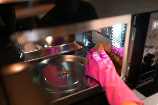 Gloved hand wiping down the interior of the microwave