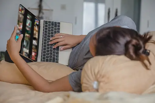 Woman lying on her side in bed using a laptop 