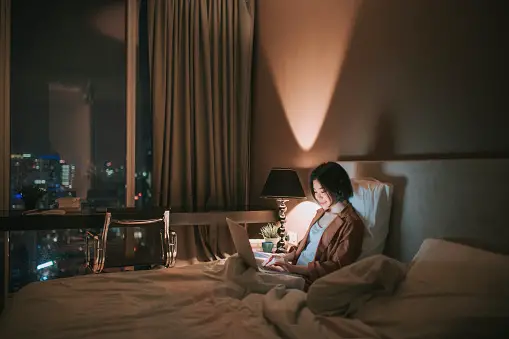 Woman on laptop in dimly lit bedroom
