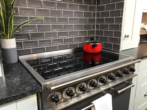 modern kitchen with red pot on the stove, plant on counter and modern dark grey backsplash