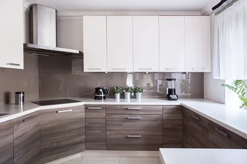 White upper kitchen cupboards, brown lower cupboards, plants and coffee maker on countertop