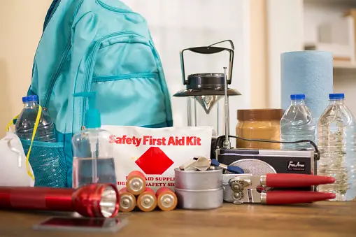 Light blue Go bag surrounded by safety supplies, such as a first aid kit, bottled water, paper towels, flashlight